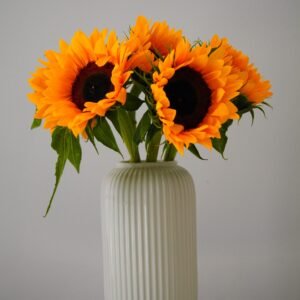 Bright sunflowers in a ribbed vase on a neutral background create an elegant still life.